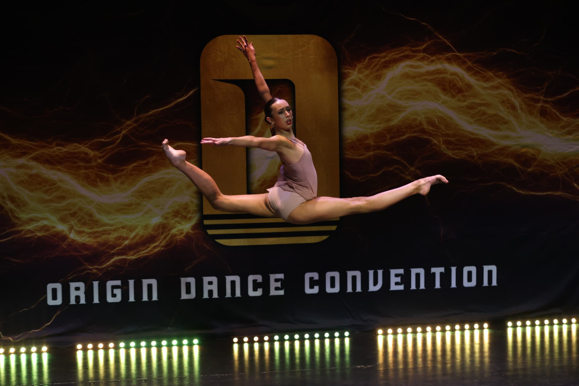 Origin competitor performing a leap on stage in front of the Origin Dance Convention backdrop